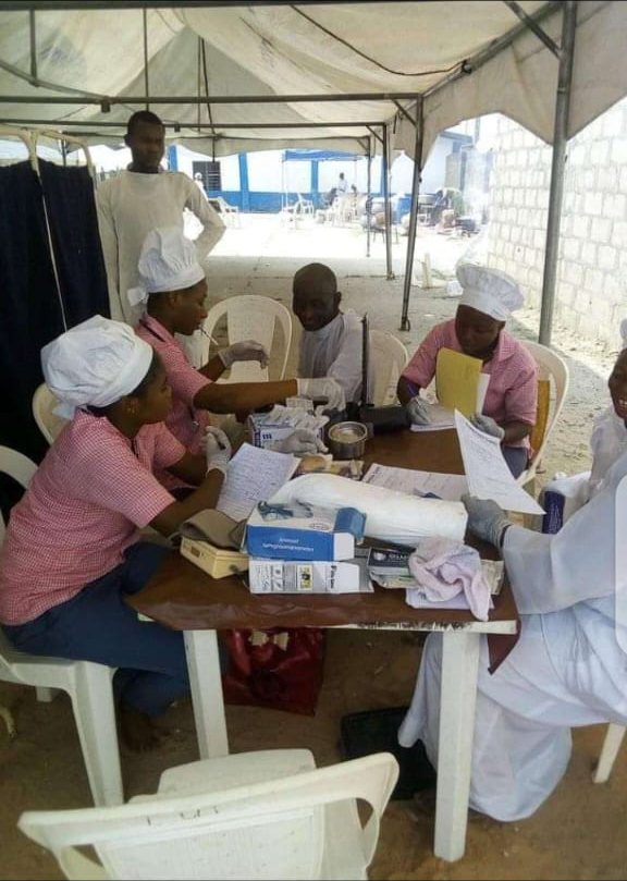 Nurses and staff of Olumayowa Nursing Home seated around a table under a canopy at a community outreach, working through records and screening equipment.