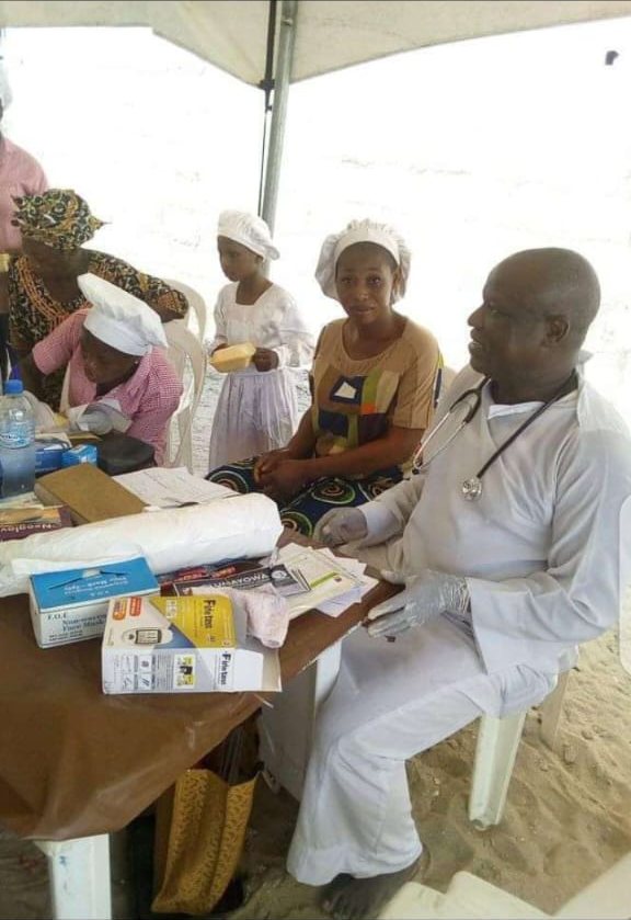A doctor with a stethoscope in conversation with patients seated beside him at the outreach table.